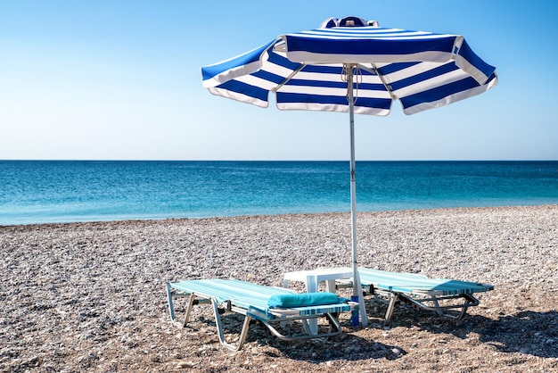 Puste leżaki pod parasolem na kamienistej plaży Morze w tle