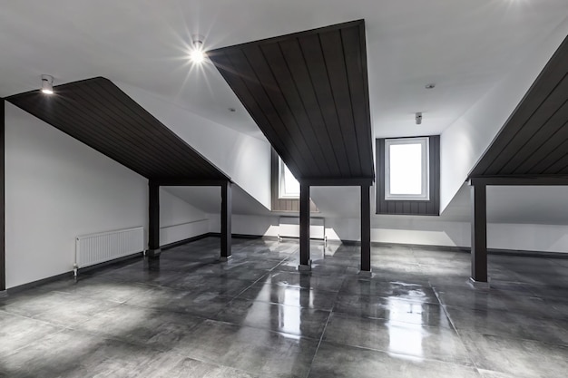 Puste nieumeblowane wnętrze mansardowego loftu z drewnianymi kolumnami i mokrą betonową podłogą na poziomie dachu w kolorze czarno-białym