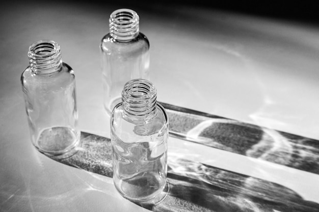 Puste szklane butelki spod kosmetyków rzucają cień na biały stół