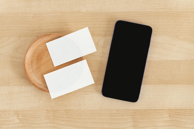 Puste wizytówki i inteligentny telefon na drewnianym stole biurowym Wizytówka i telefon komórkowy Mock Up