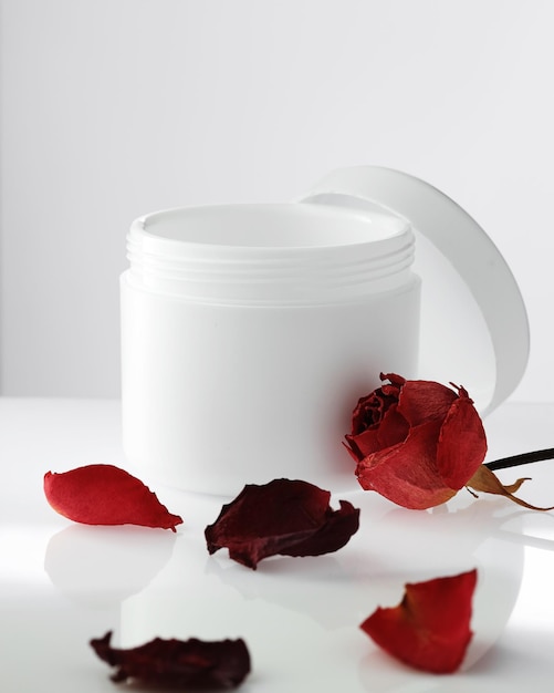 Pusty Biały Plastikowy Słoik Z Pokrywką Otwartą Na Jasnym Tle Płatki Czerwonych Róż Kosmetyki Odmładzające