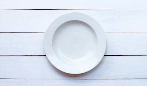 Pusty biały talerz ceramiczny na białym drewnianym na białym tle. Skopiuj miejsce