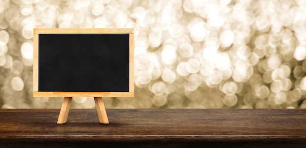 Pusty blackboard na drewno stole z plamy abstrakcjonistycznego błyskotania tła bokeh złocistym światłem