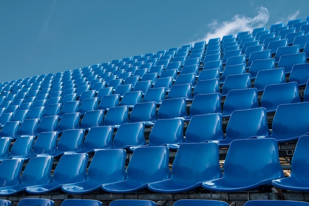 Pusty błękitny siedzenie w stadionie futbolowym z niebieskim niebem