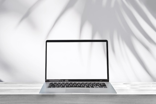 Zdjęcie pusty ekran laptopa na drewnianym stole z cieniem dłoni na białym tle ściany cementu i przestrzeni kopii