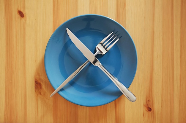 Pusty i czysty niebieski talerz z widelcem i nożem na drewnianym stole