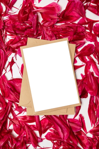 Zdjęcie pusty papier i koperta z płatkami czerwonych piwonii na szaro