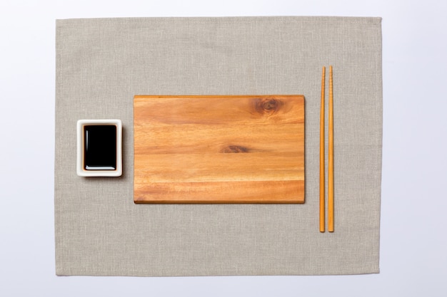 Pusty prostokątny brązowy drewniany talerz z pałeczkami do sushi i sosu sojowego na szarej serwetce