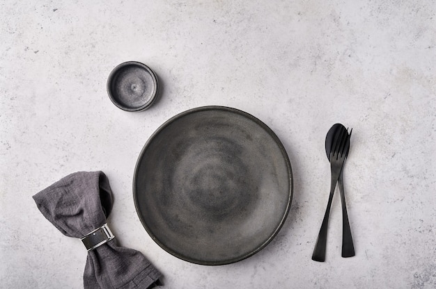 Pusty talerz sos łódka łyżka widelec serwetka w pierścieniu ciemne naczynia kuchenne ustawione na jasnoszarym stole