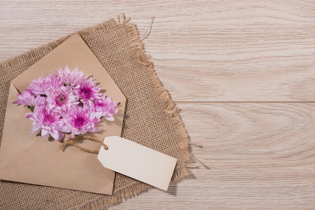 Pusty znacznik białego papieru z brązową kopertę i różowe kwiaty na drewnianym stole.