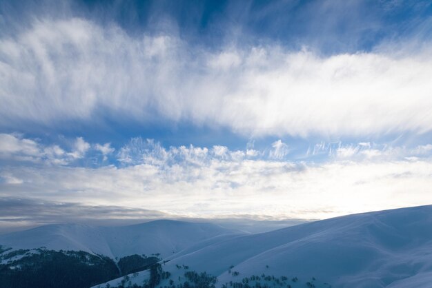 Puszyste chmury schronią się pod białym śniegiem osłonięte lasami i pięknymi górami