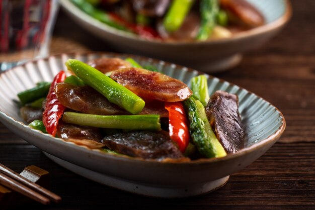Pyszna pikantna domowa smażona chińska wędzona kiełbasa ze szparagami na ciemnym drewnianym stole na posiłek.