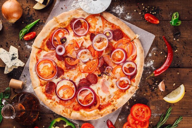 Pyszna pizza leżąca na drewnianym stole otoczona świeżymi składnikami