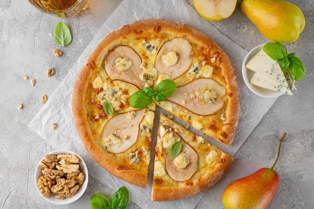 Zdjęcie pyszna pizza z gruszkami, gorgonzola, serem, orzechami włoskimi i bazylią na szarym tle betonowym