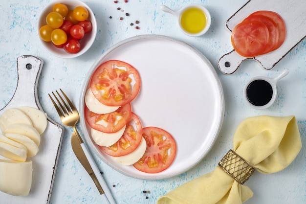 Pyszna Sałatka Caprese Z Dojrzałymi Pomidorami I Mozzarellą, świeżymi Liśćmi Bazylii, Oliwą I Sosem Balsamicznym. Włoskie Jedzenie. Widok Z Góry Leżał Płasko Na Niebieskim Tle