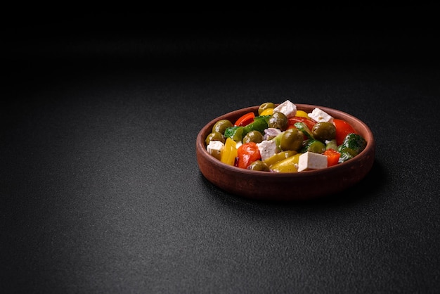 Pyszna świeża soczysta sałatka grecka z serem feta, oliwkami, pomidorami, ogórkiem, pieprzem, solą i przyprawami na ciemnym betonowym tle
