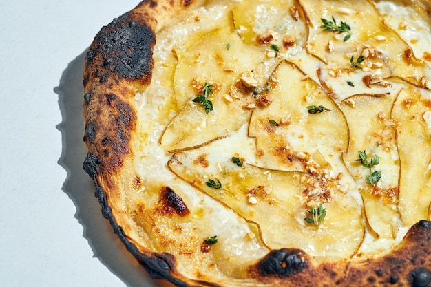 Pyszna włoska pizza opalana drewnem z kremowym sosem, orzechami nerkowca, gruszką, mozzarellą i gorgonzolą na szarej powierzchni. Ostre światło.