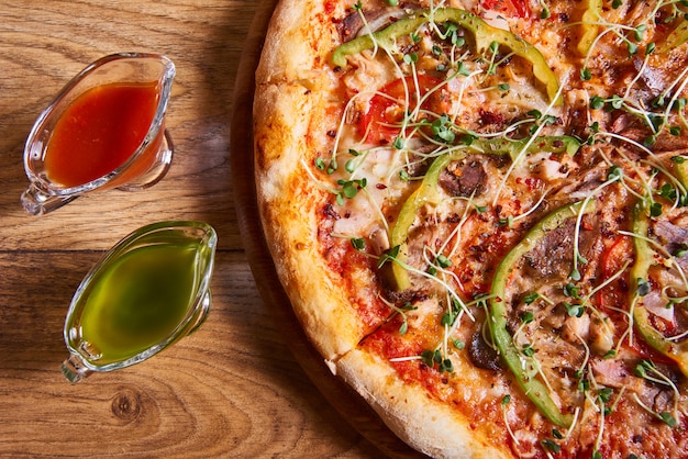 Pyszna włoska pizza podawana z sosem pomidorowym i czosnkowym na drewnianym stole. Widok z góry, z bliska
