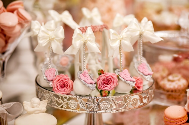 Pyszne desery w weselnym candy barze w strefie bufetowej: cake pops ozdobiony aniołkami i kameą oraz świeże pączki róż.