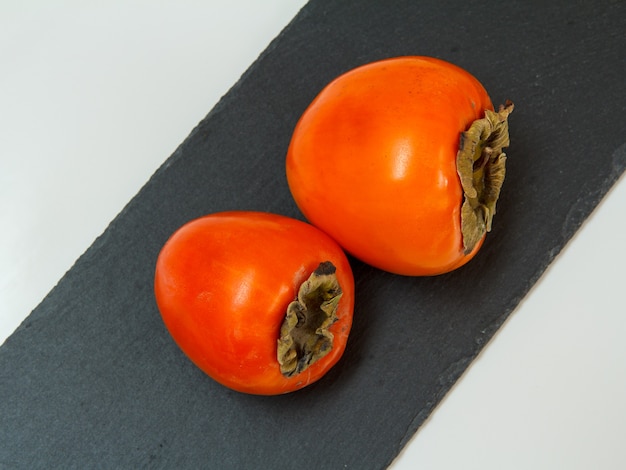 Pyszne dojrzałe owoce persimmon na czarnej kamiennej desce do krojenia