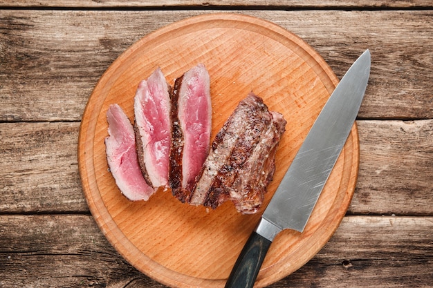 Pyszne mięso z grilla pokrojone na czarny łupek podawane na rustykalnym drewnianym stole, widok z góry.
