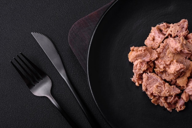 Zdjęcie pyszne mięso z tuńczyka w puszkach na czarnym talerzu ceramicznym na ciemnym betonowym tle