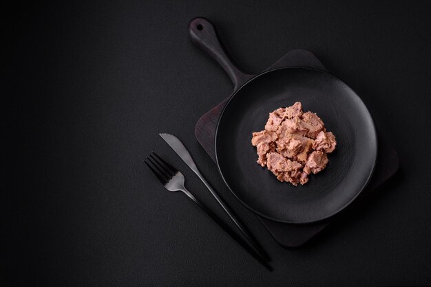 Pyszne mięso z tuńczyka w puszkach na czarnym talerzu ceramicznym na ciemnym betonowym tle