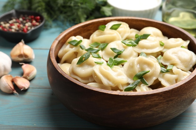 Pyszne pelmeni z zieloną cebulą w misce na jasnoniebieskim drewnianym stole