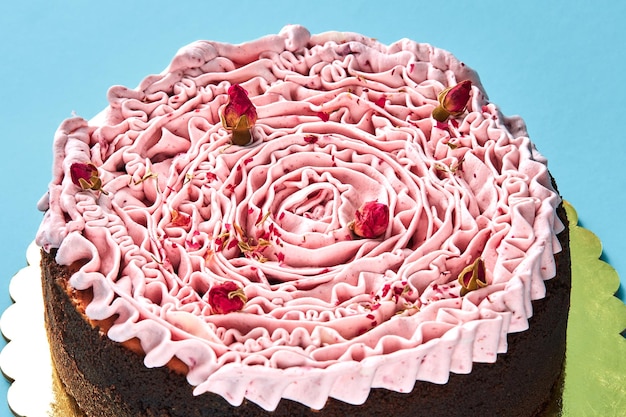Pyszne różowe ciasto ozdobione małymi suszonymi pączkami róży stojącymi na złotym stojaku na niebieskim tle studia