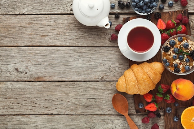 Pyszne śniadanie w tle. Smaczne rogaliki, musli i świeże słodkie organiczne jagody na poranne posiłki na rustykalnym drewnianym stole z miejsca na kopię. Widok z góry na bogate codzienne odżywianie