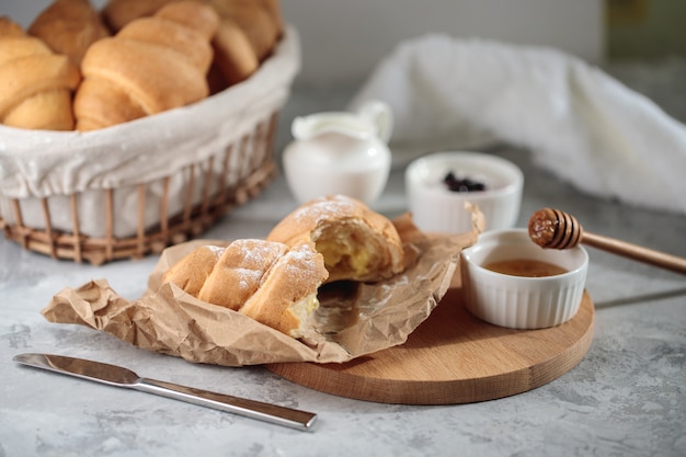 Pyszne śniadanie, zbliżenie. Łamany rogalik ze śmietaną leży na drewnianej desce, z miodową miską i dzbankiem śmietany.