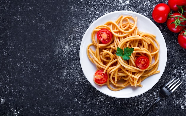 Pyszne spaghetti z natką pietruszki, pomidorkami i sosem pomidorowym na talerzu. Włoskie jedzenie i makaron. Widok z góry