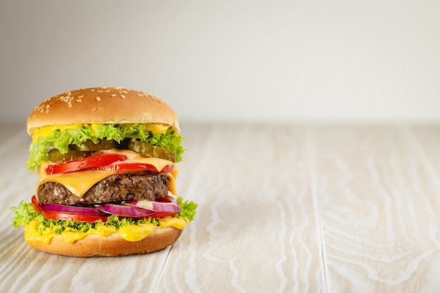 Pyszny burger z mięsem, serem, kapiącym sosem i warzywami na białym drewnianym tle rustykalnym z miejscem na tekst. Świeżo zrobiony smaczny hamburger, miejsce na zbliżenie i kopiowanie
