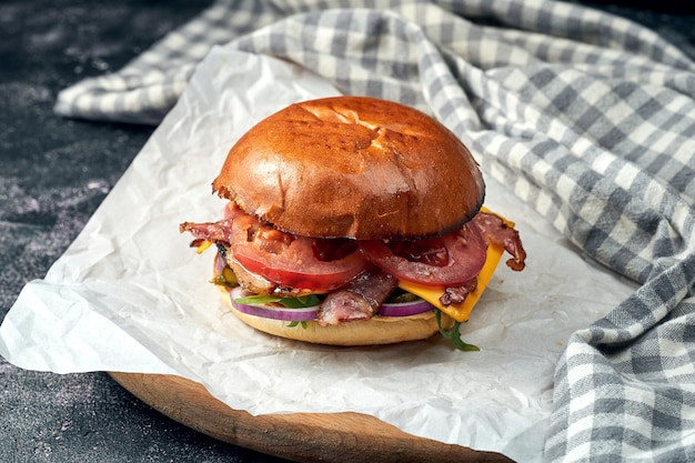 Zdjęcie pyszny burger z wołowiną, pomidorami, sałatą, topionym serem i boczkiem na białym pergaminie. ciemna powierzchnia. amerykańskie fast foody