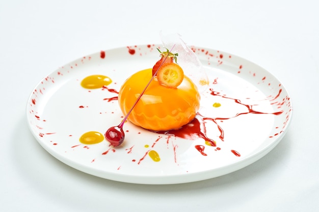 Pyszny deser - mus z mango z nadzieniem jagodowym i dekoracją karmelowo-jagodową w białym talerzu. Na białym tle na szarej powierzchni.