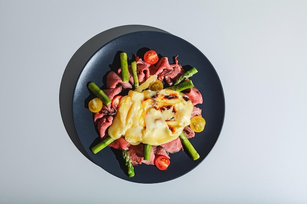 Pyszny ser raclette podawany na rostbefie z pomidorami i daniem ze szparagami