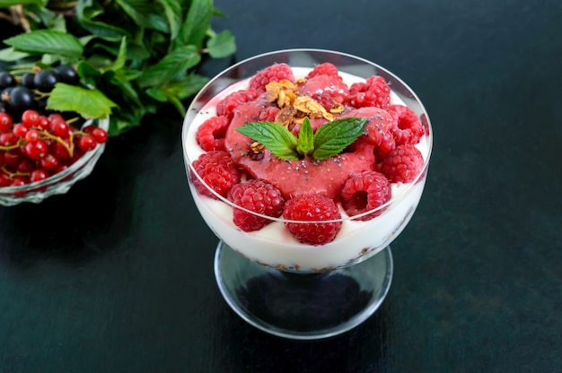 Pyszny zdrowy deser: jogurt, świeże jagody, muesli, sos malinowy na czarnym.