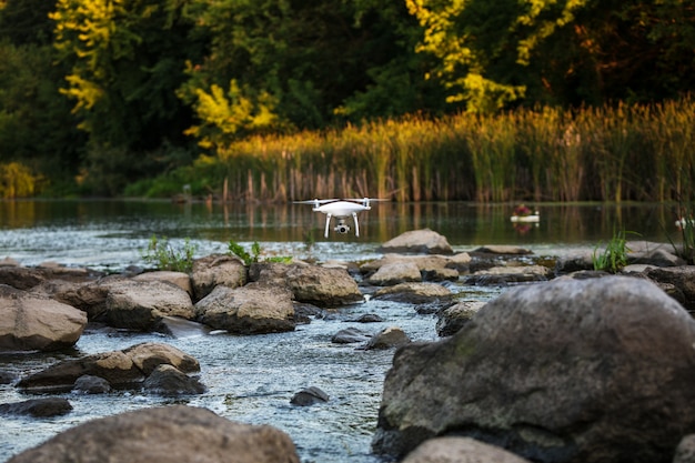 Quadcopter drone latający z kamerą nad jeziorem.