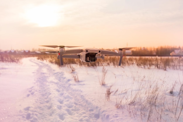 Quadkopter dron lecący nad zaśnieżonym polem zimą o zachodzie słońca