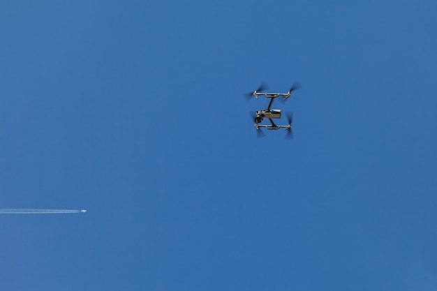 Quadrocopter zawieszony w powietrzu na tle błękitnego nieba i latającego samolotu