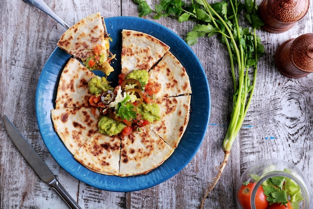 Quesadilla z kuchni meksykańskiej z widokiem z góry podawana na niebieskim talerzu z guacamole, salsą i jalapenos