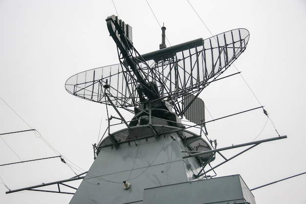 Radar na okręcie wojennym na metalowej konstrukcji na tle szarego nieba. Dużo drutów i części metalowych. Deszczowa ponura pogoda.