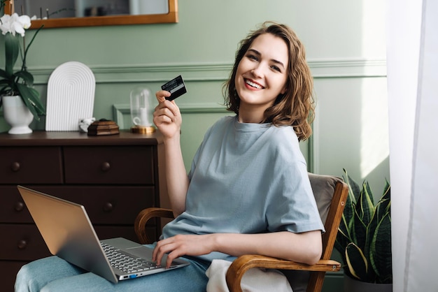 Radość zakupów online Młoda kobieta zachwycona kartą kredytową i laptopem Wesoła kobieta robiąca zakupy