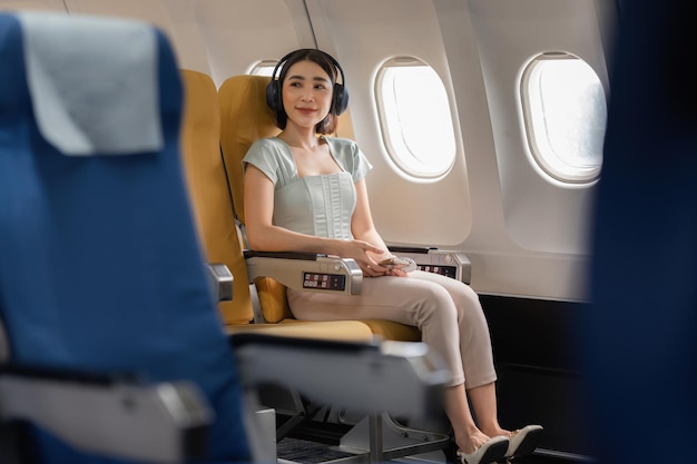 Radosna Azjatka siedzi w samolocie i słucha muzyki podczas podróży