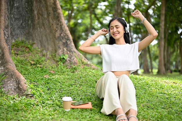 Radosna Azjatycka kobieta ciesząca się słuchaniem muzyki przez słuchawki podczas relaksu w parku