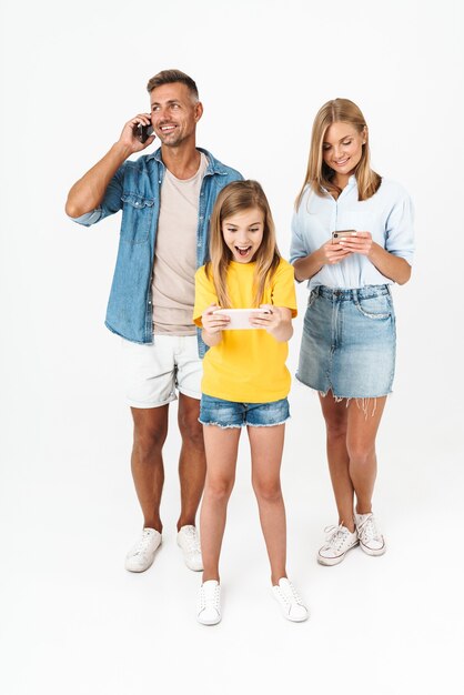 radosna kobieta i mężczyzna z małą dziewczynką uśmiechnięci podczas wspólnego używania telefonów komórkowych na białym tle