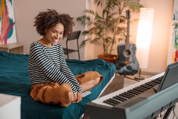 Radosna kobieta muzyk siedząca przy syntezatorze w domu
