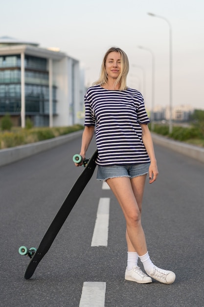 Radosna kobieta w średnim wieku szczęśliwa po jeździe na deskorolce wesoła blond kobieta s trzymająca longboard