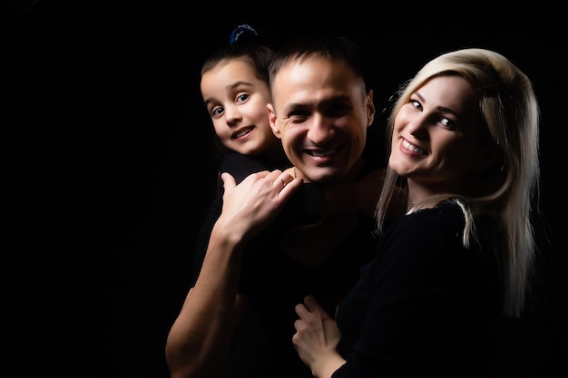 Radosna matka rodziny, ojciec i mała dziewczynka w czarnych ubraniach z ciemnym tłem. Portret rodzinny.