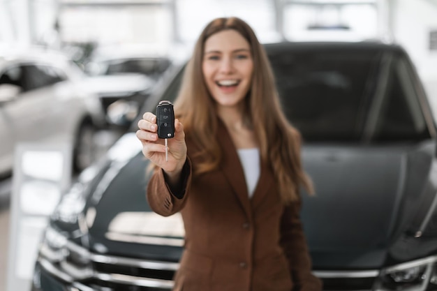 Radosna młoda kaukaska kobieta trzyma klucz od auto kupując zupełnie nowy samochód w salonie selektywnym